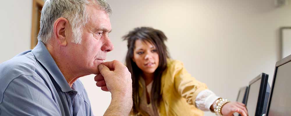 Caucasian male stares at computer screen and educator next to him points out at the screen. Education ex-offender.